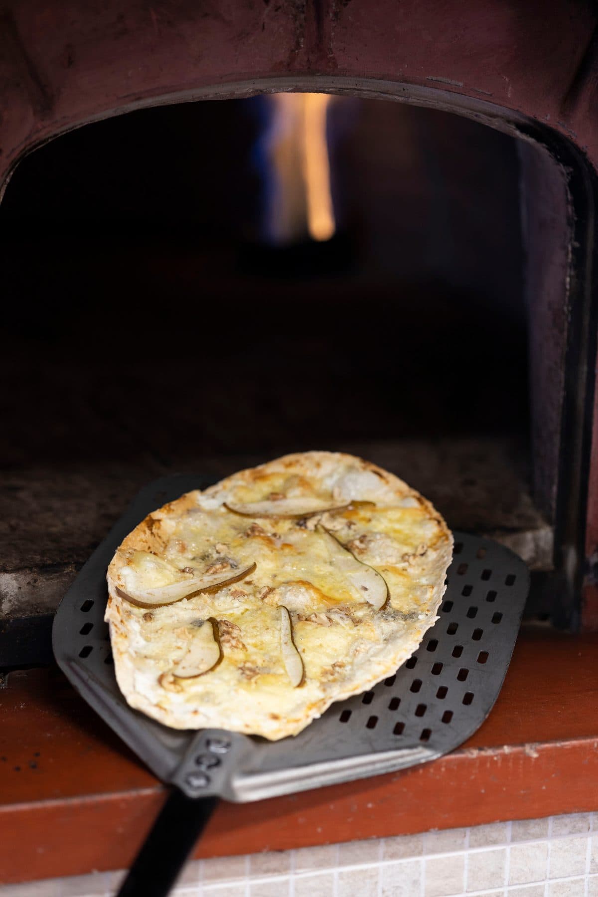 Kvit pizza på takkesteikt botn, på veg ut av vedomnen i kafeen